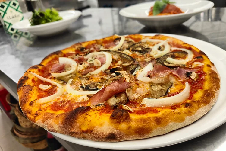 Traditionell, angerichtete Steinofen-Pizza mit frischem Parmaschinken und knackigen Pilzen und Zwiebeln aus der mediterranen Küche des Giovino-Restaurants Düren.